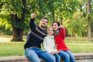 Anne ve baba kızlarını ağaçlar veya doğa arka plan karşı arasında oturup, bir şey ona göstermek, ile belirtmek ön plana parmak. Gülümseyen anne kuş küçük güzel bir kızla göster. Ebeveynlik