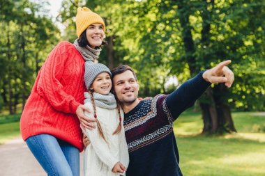 Üç aile üyeleri birlikte vakit, güzel göl Park bakmak, parmaklarıyla, keyfin yerinde olmak göstermek, hoş gülümseme. Baba, anne ve kızı beraberlik, sakin atmosferi tadını çıkarın