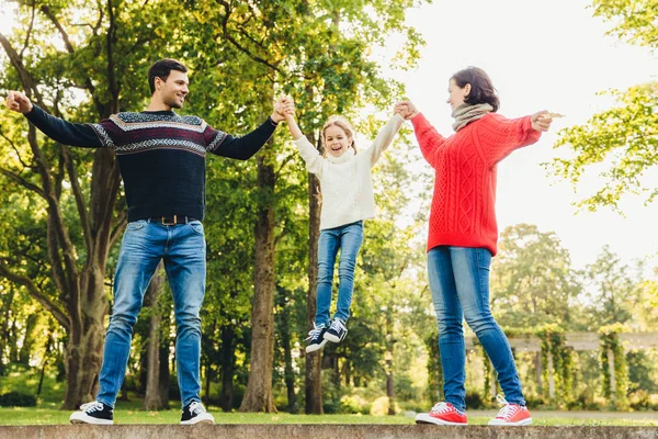 Podekscytowany, małe dziecko, że cieszę się, że czas z rodzicami, skały w ich ręce, uśmiecha się radośnie. Figlarny Urocza dziewczyna z happy expressionn, lubi spędzać czas z ojcem i matką. — Zdjęcie stockowe