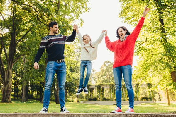 Komik eğlenceli çocuk ebeveynin ellerde, çok memnun sallamak. Annem ve babam onların küçük kızı açık havada ile oynamak. Mutlu aile kavramı. Anne çocuğun elele tutuşun. Ebeveynlik ve insanlar