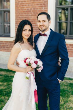 Sadece evli çift birbirinize sarılın, mutlu ifadeler varsa, birbirine yakın durmak. Güzel esmer erkek beyaz gelinlik, siyah takım elbiseli bouquete ve onun yakışıklı damat tutar