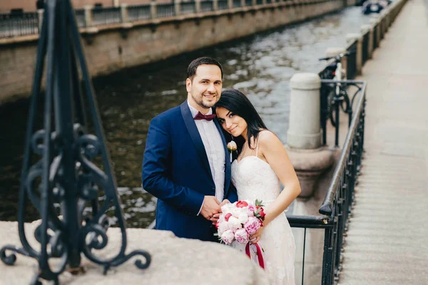 Verliebte Paare feiern ihre Hochzeit, posieren in der Nähe von Brücke und Fluss vor der Kamera, haben ein glückliches Lächeln. freudig positive Eheleute haben romantische Beziehungen. Hochzeitskonzept — Stockfoto