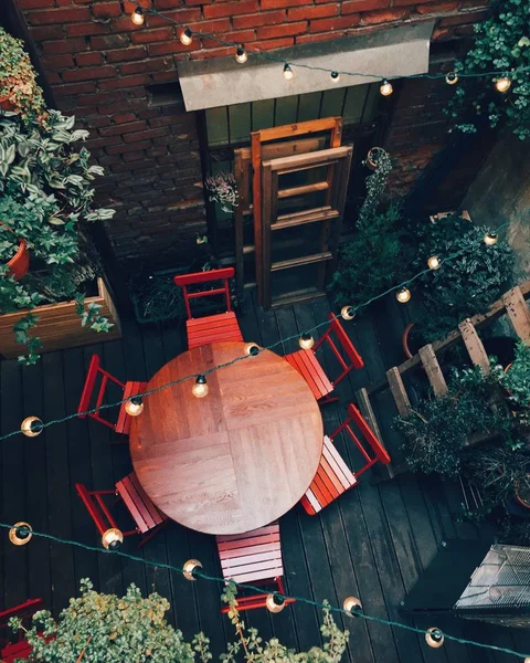 Top view of round table and chairs on wooden floor. Cozy interior of outdoor cafe with necessary furniture and garlands with light lamps. Comfort concept. Calm atmosphere — Stock Photo, Image