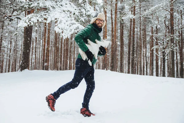 Outdoor Portret van positieve gelukkig man heeft leuke wandelingen in winter bos, geniet van de prachtige landschappen en verse koude weer, houdt van kunstmatige witte firtree, direct in de camera kijkt. Winter concept — Stockfoto