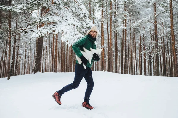 Optimistiska unga manliga klädd i varma vinterkläder, har kul utomhus i vinter skogen, andas frisk luft, kul att se mycket snö, håller atrficial fir tree i händerna. Människor, årstid, väder koncept — Stockfoto
