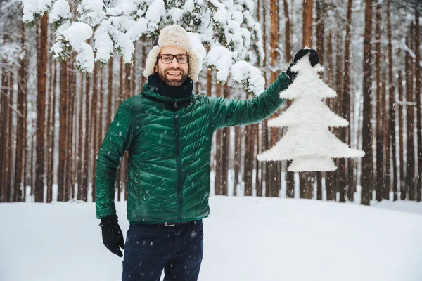 Kijk naar deze prachtige spar boom! Vrolijke bebaarde man in bont pet met oorkleppen en groene anorak, graag wandelen in winter bos, geniet van prachtige bomen en natuur landschappen. Seizoen concept — Stockfoto