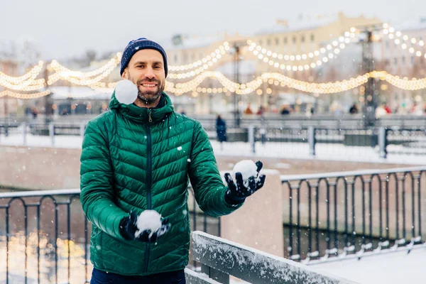 Playful smiling male juggles with snowballs throws them in air, — Stock Photo, Image