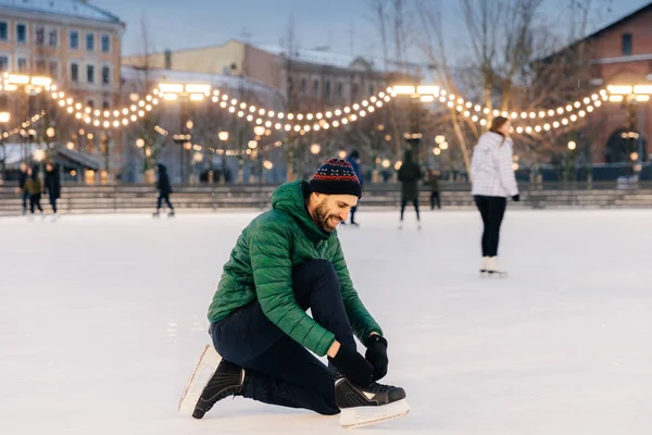 Portrait of cheerful male laces up skates as going to go skating — Stock Photo, Image