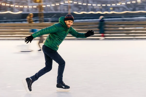 Shot of cheerful male has fun outdoor, skates on ice ring, enjoy — Stock Photo, Image