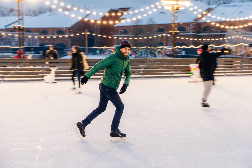 Joyful bearded man practices going skating on ice ring, has chee