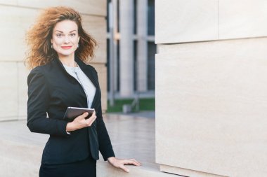 Çok iyi görünümlü erkek resmen, onun iş için gerekli olan holding dijital tablet bilgisayar giyinmiş. Kıvırcık gür saçlı çekici görünümü olması, onun iş için gidiş güzel kadın