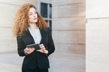 Onun çalışma günü planlama kadın girişimci kıvırcık gür saçlı resmi elbise giyiyor, modern tablet holding, dalgın bir ifadeyle bir yana, arıyorum. Dokunmatik yüzey kullanarak proje geliştirme kadın