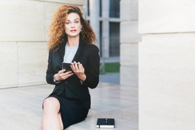 Kendine güvenen kadın serbest meslek meşgul olurken onun tablet ile çalışma, cep kitabında notlar yazma, siyah resmi giyinen, doğrudan kameraya bakıyor. Ofis çalışanı modern Gadget'ı kullanma