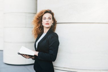 Çok şık kadın kıvırcık dalgalı saçlı siyah takım elbiseli, onun gelecek planları üzerinde düşünme cep kitabı bir kenara mesafe içine arıyorum elinde tutan giyinmiş. Moda Bayan yazma gerekli notlar