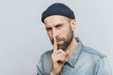 Çekici görünüm ile ciddi sakallı erkek portresi ön plana tutan parmak dilinde, görünümü gizli ifade ile sorar sessizlik tutmak ve onun gizli gri arka plan üzerinde izole kimseye söyleme