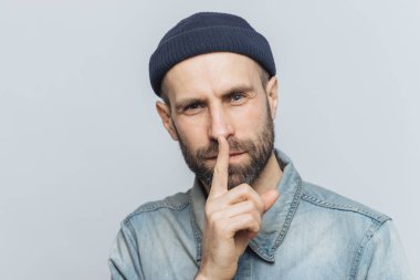 Yakışıklı adam kalın sakal ve bıyık, headshot gizli bir görünüme sahiptir, sessizlik işareti gösterir, gri arka plan üzerinde izole sessiz olun, ister. Yüze ilişkin tabir ve beden dili kavramı