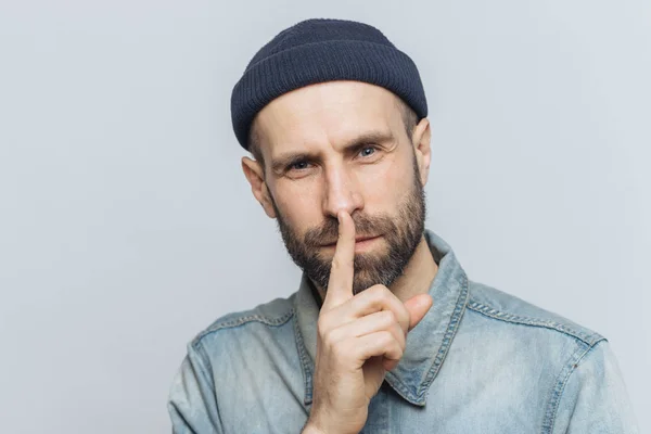 Headshot of handsome man with thick beard and mustache, has secret look, demonstrates silence sign, asks to be silent, isolated over grey background. Facial expressions and body language concept — Stock Photo, Image