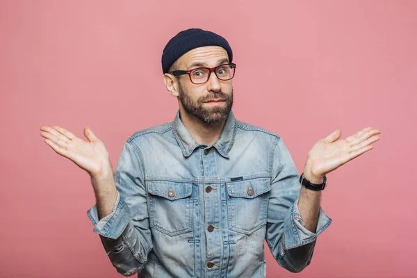 Indoor shot of hesitant bearded man shrugs shoulders, looks unce — Stock Photo, Image