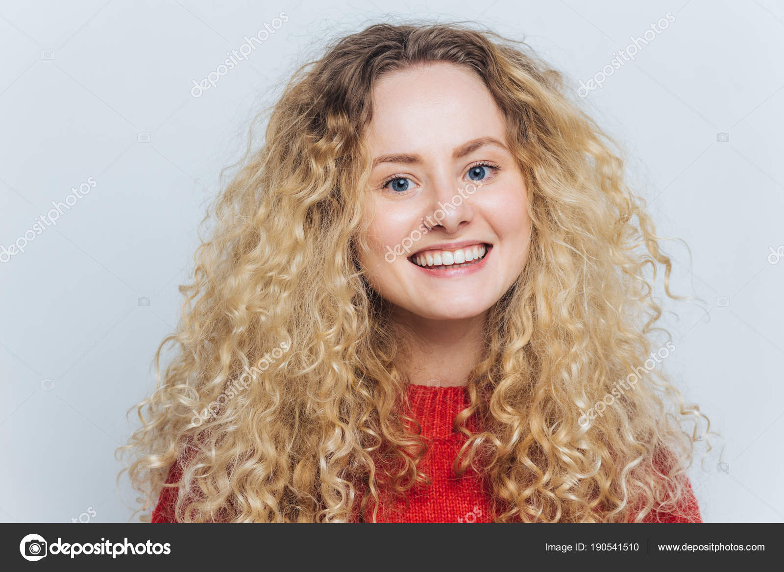 Delighted pleased adorable woman with curly blonde hair and warm blue eyes, being in good mood as recieves compliment, isolated over white background. Glad happy female smiles joyfully at camera Stock Photo Delighted pleased adorable woman with curly blonde hair and warm blue eyes, being in good mood as recieves compliment, isolated over white background. Glad happy female smiles joyfully at camera Stock Photo