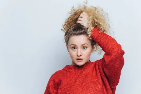 Foto interior de hermosa hembra de ojos azules en suéter rojo, posa con expresión aturdida, vestida con suéter rojo, aislada sobre fondo blanco. Me preguntaba si la joven no cree en algo. — Foto de Stock