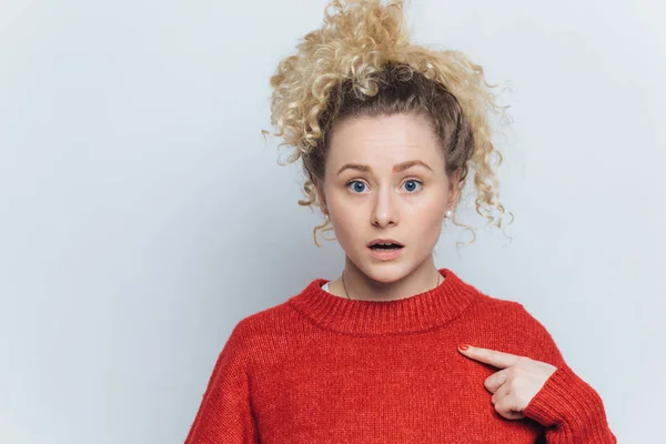 Zszokowany oszołomiony młoda kobieta z zaskoczony wyrażenia, wskazuje na puste czerwony sweter, advertizes nowy strój, pozuje na tle białego studia z kopia miejsce na tekst promocyjny. — Zdjęcie stockowe