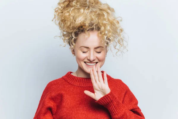 Portret szczęśliwy zachwycony młoda kobieta z wesoły wyrażenie, utrzymuje oczy zamknięte i miły uśmiech, ubrany w czerwony sweter, podnosi rękę i gesty w studio, na białym tle nad białym tle — Zdjęcie stockowe