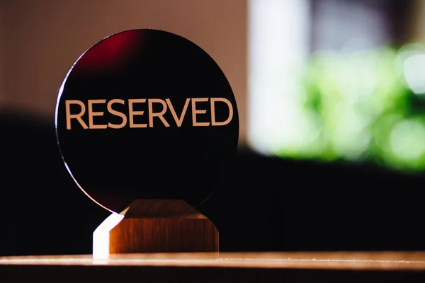 Table sign denoted reserved table in restaurant stands against blurred cafe background. Reservation concept. A tag of reservation. Beige on wooden table. — Stock Photo, Image