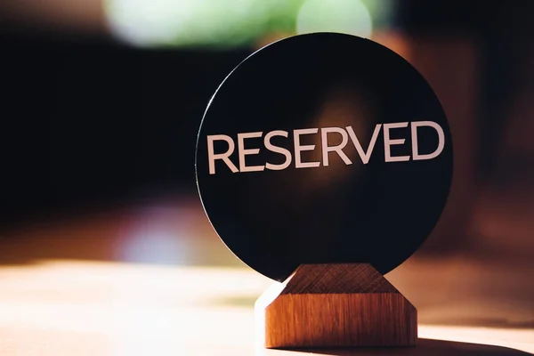 Cartel de madera reservado en restaurante en la mesa. Mesa lista. Letras mayúsculas. Asiento de reserva en cafetería. Insignia de reserva. Logotipo reservado. Imagen tonificada y fondo borroso . — Foto de Stock