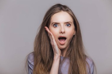 Hayret sürpriz esmer erkek portresi yaygın olarak açıldı ağız tutar, beklenmedik Haberler, bakışları ile hayrete ifade, gri studio arka plan üzerinde izole kamera almak beklemiyor