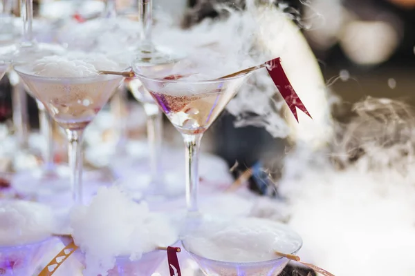 Glasses of champagne with smoke around. Chemical reaction of dry ice with water. White fog from alcoholic cocktail. Recreation and celebration concept