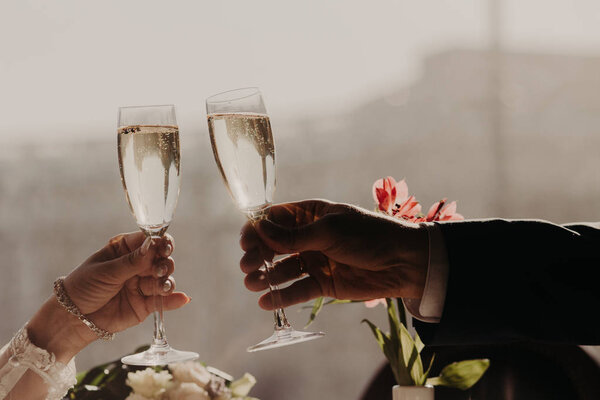 Woman`s and man`s hands hold glasses of alcoholic beverage, clink glasses, celebrate their wedding day. Leisure, celebration, drinks, holidays and people concept