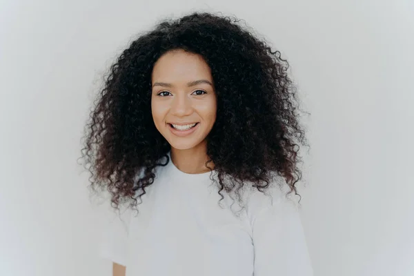 Felicità, benessere ed emozioni positive. Headshot di piacevole signora dall'aspetto con capelli croccanti, sorrisi e risate, ha una pelle sana, indossa maglietta casual, modelli contro la parete bianca dello studio . — Foto Stock