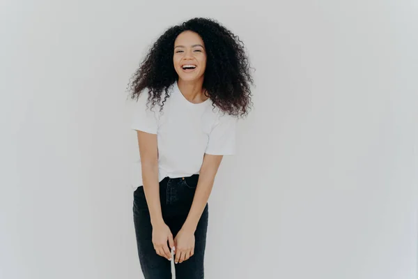 Photo studio de joyeuse femme afro-américaine rit joyeusement, vêtue de vêtements décontractés, se sent bien, pose sur fond blanc avec un espace vide pour votre contenu publicitaire, se sent énergique — Photo