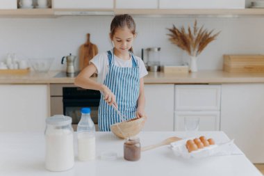 Önlüklü küçük tatlı bir kız, malzemeleri çırpıcıyla karıştırır, yumurta, süt, un kullanır, yeni tarifler dener, mutfağın içinde durur, lezzetli kurabiyeler veya fırın hazırlar, nasıl pişirileceğini öğrenir..