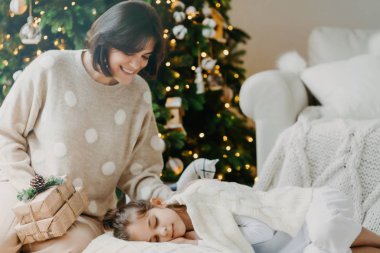 Evde Xmas 'ın tadını çıkarıyorum. Sevecen genç bir anne, uyuyan kızının yanında poz verir, sürpriz yapar, hediyeler tutar, mucizelere inanır. Sihirli ve tatlı bir an. Aile tatili kavramı