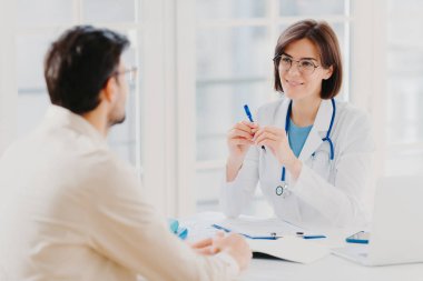 Erkek hasta klinikte doktoru ziyaret eder, sorunlarını anlatır, hastalıktan bahseder. İlgili kadın doktor tıbbi geçmişine notlar yazar, reçete yazar, hastaların sağlık sorunlarını dinler.