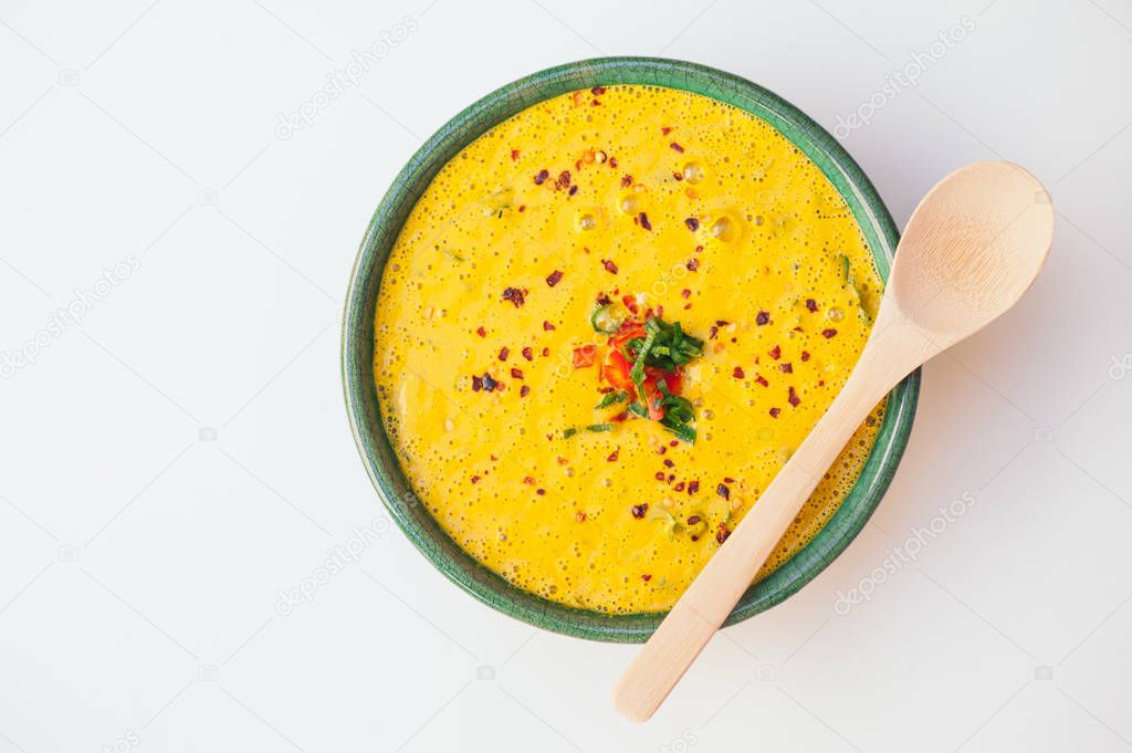 Hot creamy delicious soup with greenery and vegetables, wooden spoon on bowl, isolated over white background. Coconut curry soup. Fresh disn. Healthy eating concept