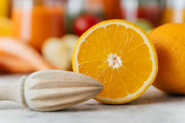 Close up de laranja fresca fatiada e espremedor de madeira. Citrinos suculentos em fundo desfocado. Foco seletivo. Conceito de alimentação saudável — Fotografia de Stock