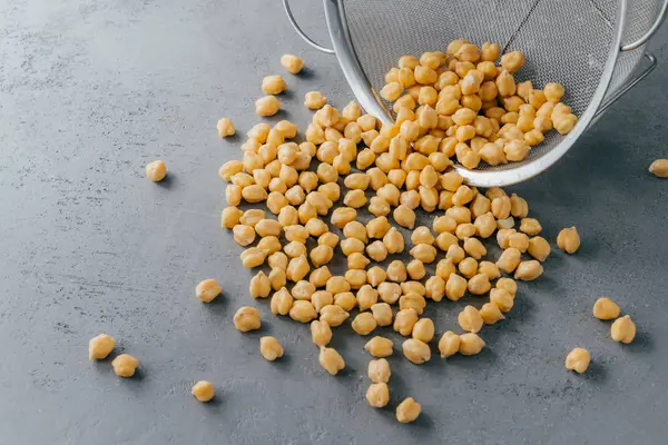 栄養価の高い乾燥したひよこ豆は、灰色の背景にふるいからこぼれました。高エネルギー食品。健康的なスナック。タンパク質有機製品 — ストック写真