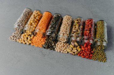 Various raw grains in glass jars poured out on grey background. Food storage and healthy nutrition concept. Organic ingredients and recipe