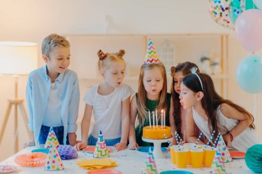 Küçük çocuklar doğum günü partisini kutlar, pastaya mum üfler, şenlik masasında toplanır, keyifli vakit geçirir, birlikte vakit geçirir, dilek tutar, parti şapkaları takar, şişmiş balonlarla içeride poz verir.