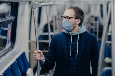 Toplu taşımacılıkta önleme, salgın hastalıkların korunması için sağlık bilinci. Genç adam şehir treniyle seyahat ederken tıbbi maske takıyor ve kendini virüsten koruyor. Avrupa 'da Covid-19 salgını.