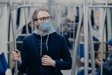 Koronavirüs salgını sırasında koruyucu maske takan, toplu taşımada poz veren, hastalığın üstesinden nasıl gelineceğini düşünen düşünceli genç adam. Virüs koruması, karantina konsepti.