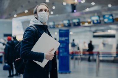 Gezgin adam havaalanında koruyucu tek kullanımlık tıbbi maske takıyor. Yurtdışından geliyor. Coronavirus 'un yayıldığı, sırt çantası taşıdığı, sağlığıyla ilgilendiği, virüsten korunduğu ve uçuşunu ertelediği yerden.