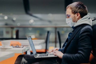 Laptop bilgisayarında serbest çalışan klavyelerin yan görüntüsü, uzaktan çalışıyor, virüs salgını yüzünden karantina sırasında koruyucu maske takıyor, kahve dükkanında poz veriyor, bulaşıcı hastalıklar uyarısında bulunuyor