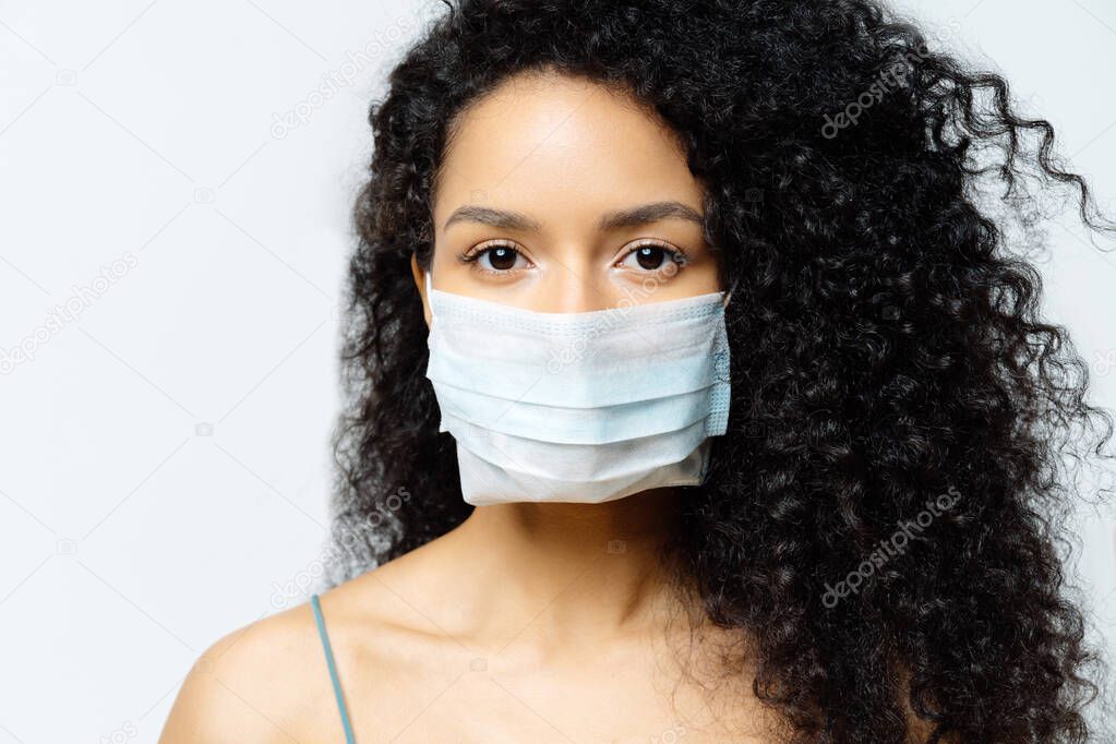 Serious Afro American woman tries to stop virus and epidemic disease, stays at home during infectious outbreak, wears medical mask, isolated on white background, being hospitalized, diagnosed