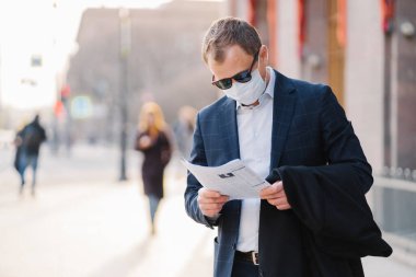 Coronavirus hastalığı. Ciddi bir erkek bankacı gazete okur, dünyadaki salgın hastalıkları öğrenir, koruyucu maske takar, virüsün yayılmasını önler, sokakta durur..