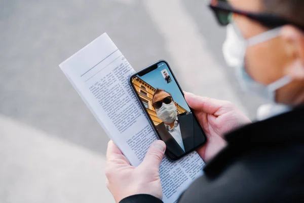 Kimliği belirsiz adamın görüntüsü modern cep telefonuyla video görüşmesi yapıyor, virüs yayılırken koruyucu maske takıyor, koronavirüsü önlemek için sadece uzaktan iletişim kuruyor, gazete tutuyor.