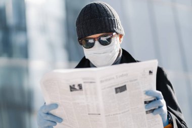 Avrupalı bir adamın koruyucu maske ve eldiven taktığı, şehirde gezdiği, farklı ülkelerdeki virüs salgını hakkında makaleler okuduğu, Coronavirus yayılması sırasında koruyucu önlemler aldığı fotoğraf