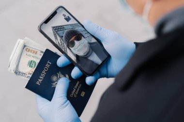Tanımlanamayan bir adam video görüşmesi yapıyor, arkadaşıyla konuşuyor koruyucu lastik eldivenler takıyor, pasaportu parayla birlikte elinde, Coronavirus salgını sırasında ülkeyi terk edecek. Sosyal uzaklık kavramı